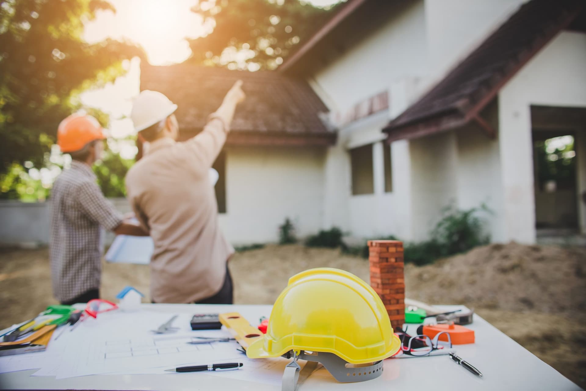 Deux techniciens MS FIBRE en repérage devant une maison en chantier, plans et casque de sécurité au premier plan